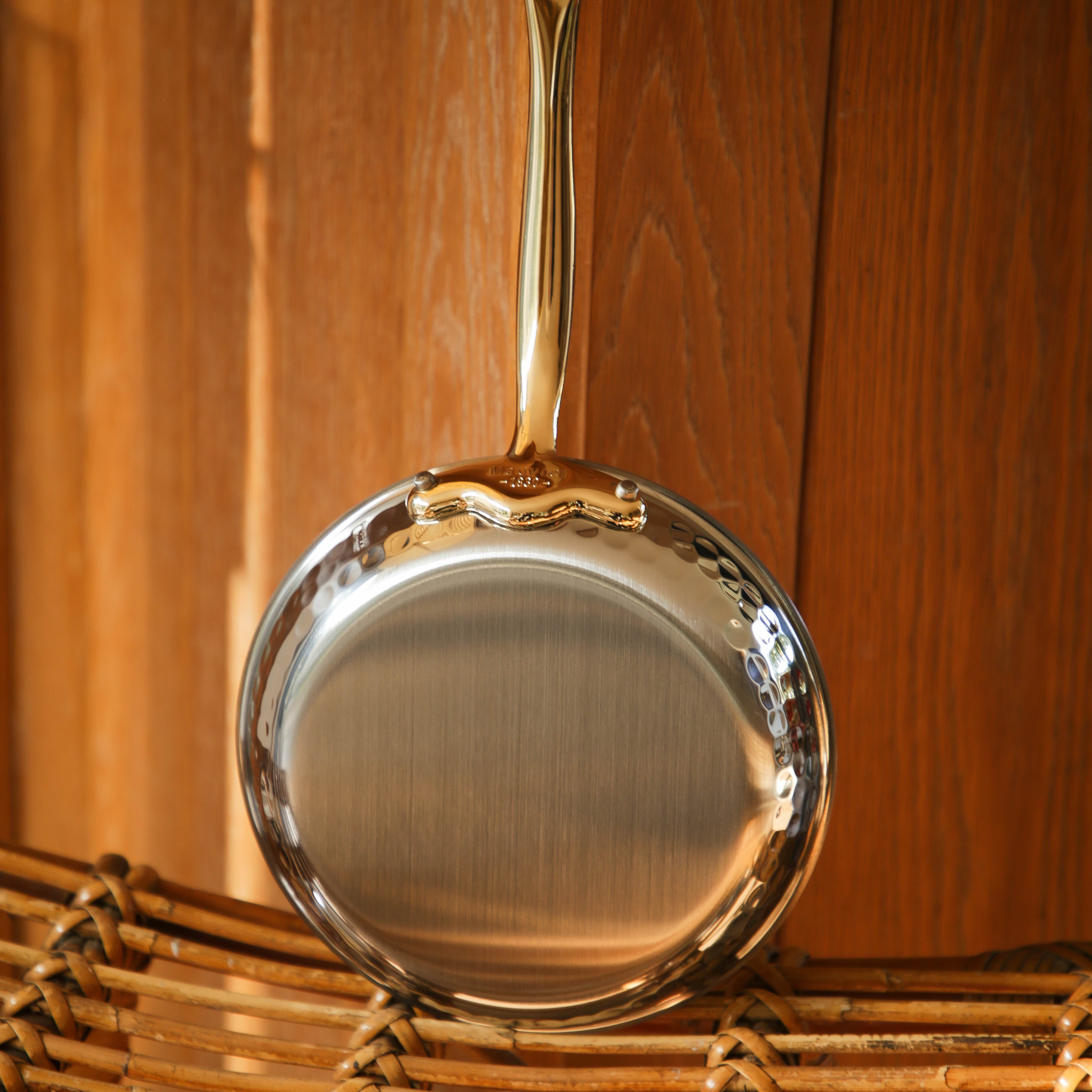 Mauviel M'ELITE B hammered 5-ply frying pan set with brass handles, shown in a lifestyle kitchen setting.