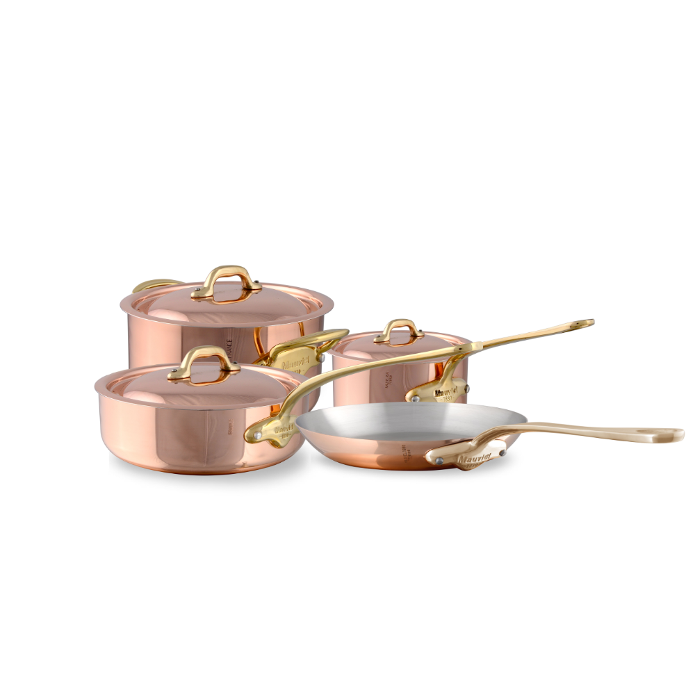 Mauviel M'Heritage M'150 B 7-piece copper cookware set with brass handles, including saucepans and pots on a kitchen countertop.