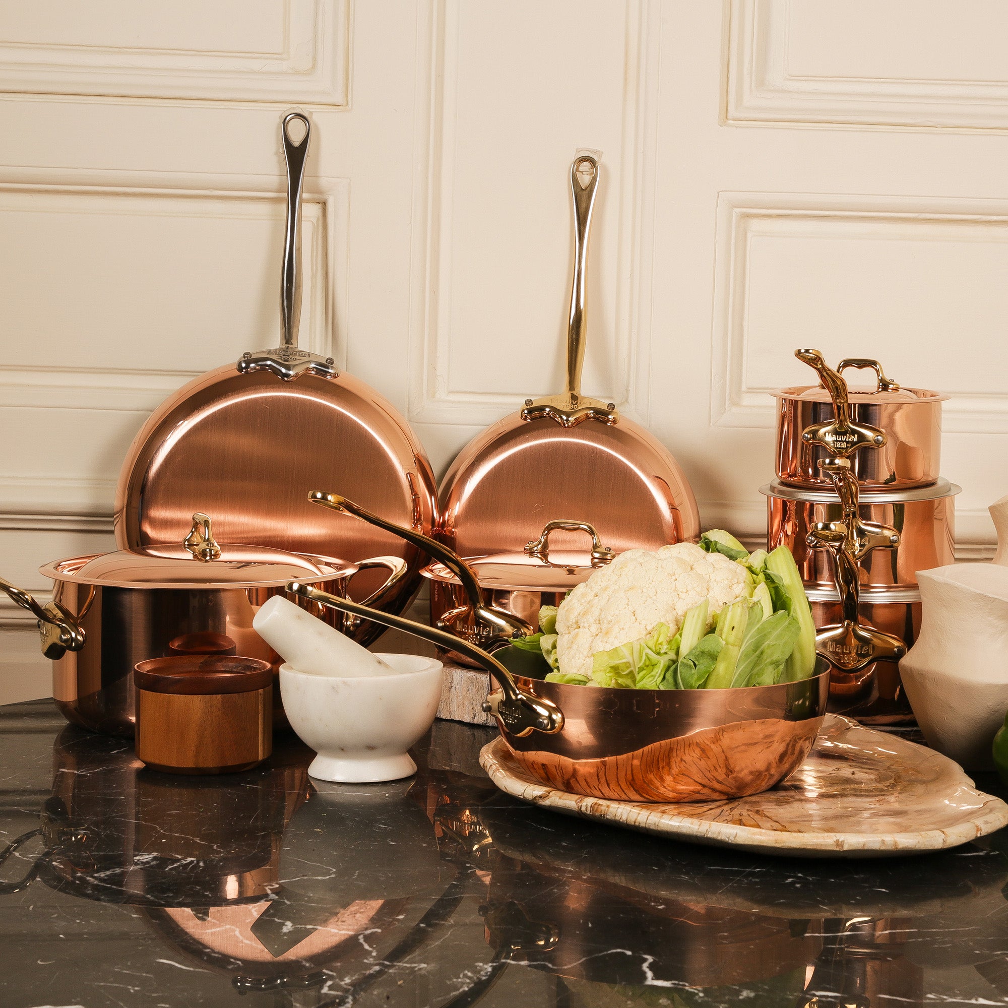 Mauviel M'Heritage M'150 B copper oval frying pan set with two pans and brass handles, shown on a kitchen countertop.