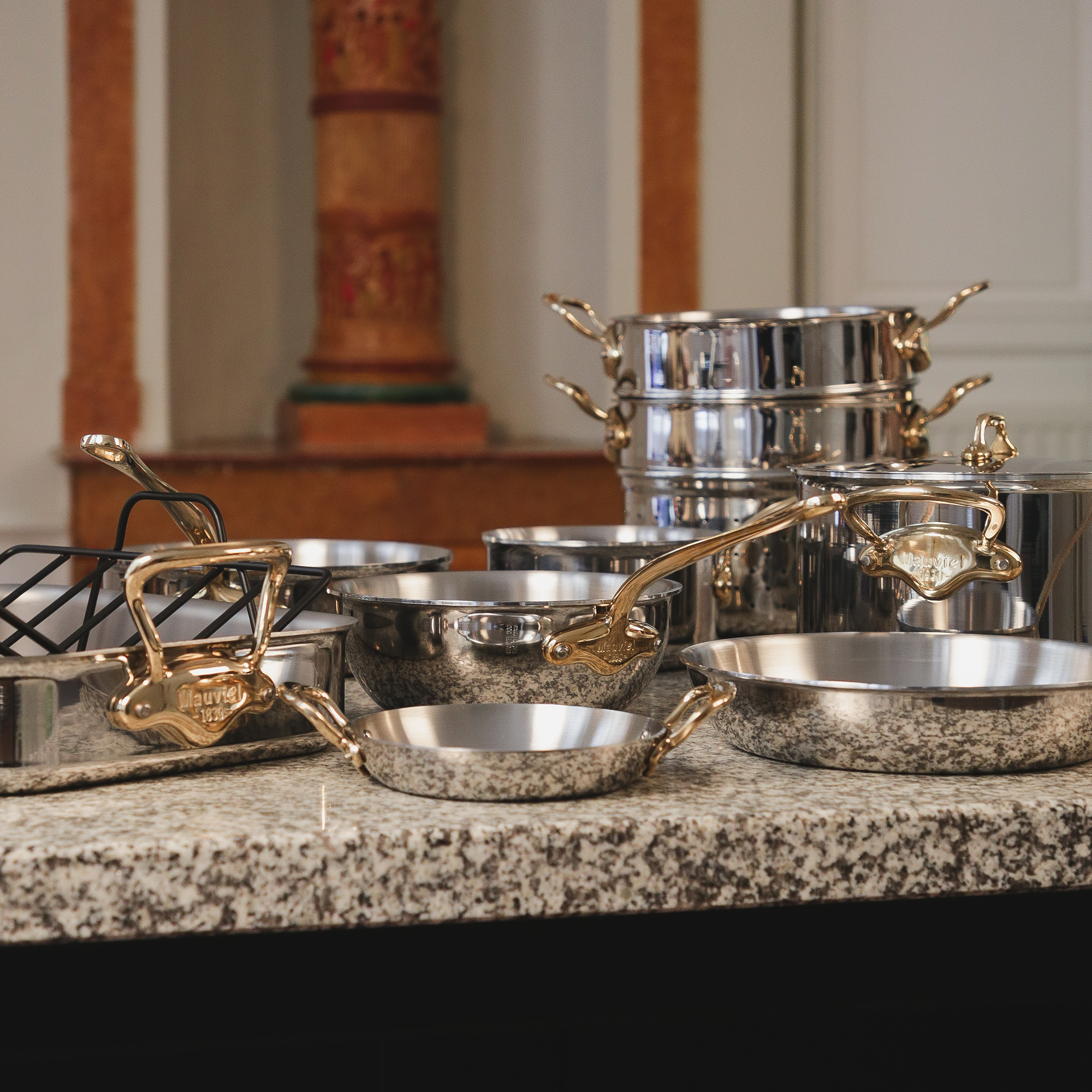 Mauviel M'COOK 5-ply stainless steel frying pan set with brass handles, showing two pans with polished surfaces and sturdy handles.