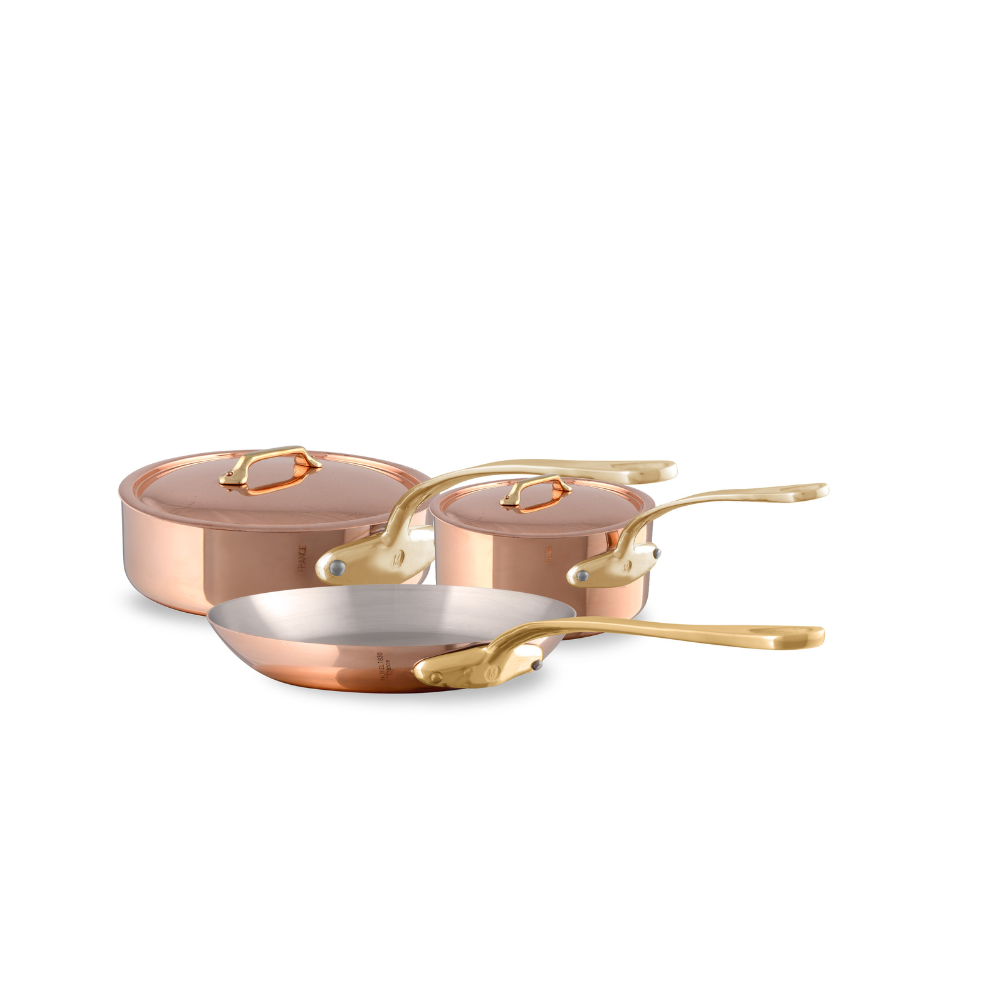 Mauviel M'Heritage M'200 B 5-piece copper cookware set with brass handles, including saucepans and a stockpot, on a kitchen countertop.