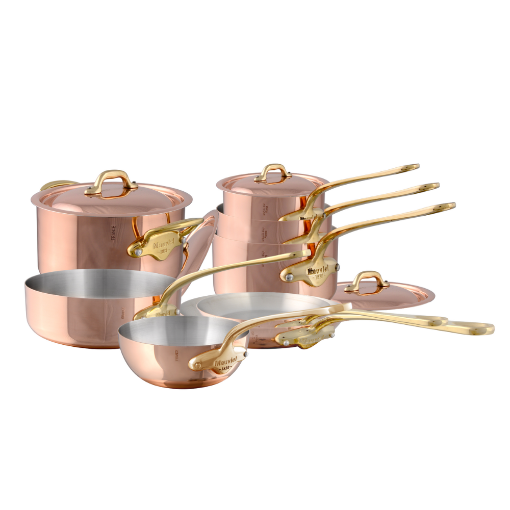 Mauviel M'Heritage M'150 B 12-piece copper cookware set with brass handles, including pots and pans arranged on a kitchen counter.